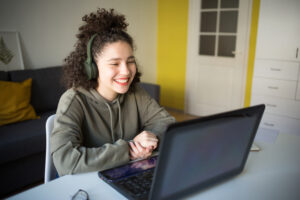 happy mixed rase girl sits at computer screen laptop. student talks over Internet.